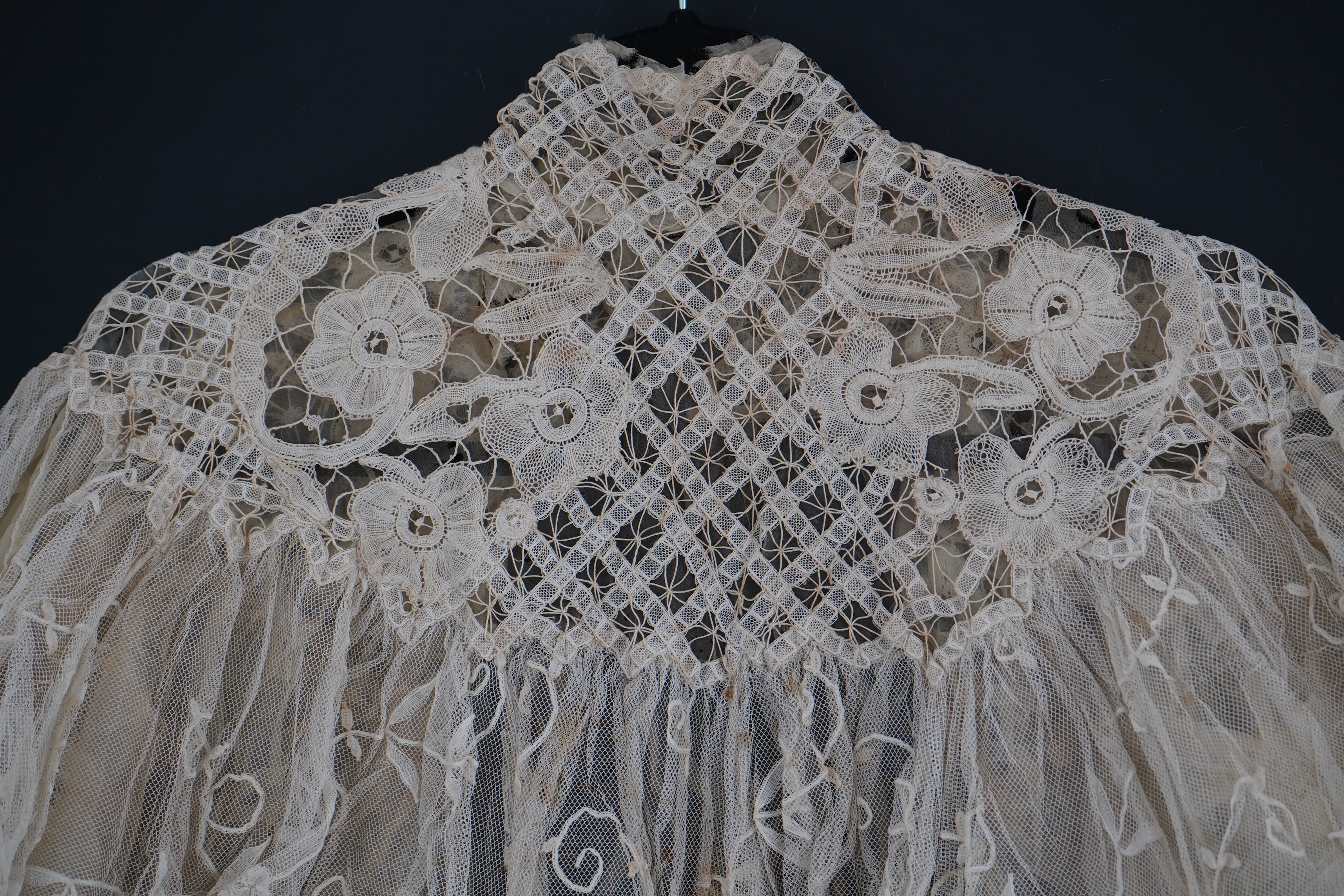 An Edwardian high collared cream tape lace wedding over blouse, made with a deep net frill and cream chiffon rose detail hanging from lower edge, top of collar to rose detail at the front 46cm. Condition - fine silk chif